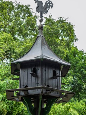 Parlak bir gökyüzüne karşı Metal Horoz Weathervane 'i ile süslenmiş Koyu Ahşap Kuş Evi.