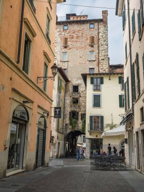 Uzun bir ortaçağ tuğla kulesinin altındaki taştan kemerin altından geçen dar bir sokak, Brescia, İtalya.