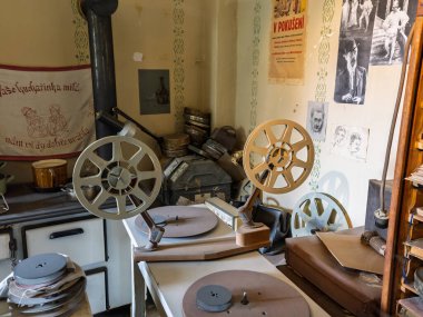 Antika film projektörü, duvarında Prag, Çek Cumhuriyeti 'nin eski posterleri olan küçük bir odada, ocağın yanındaki masada büyük makaralı..