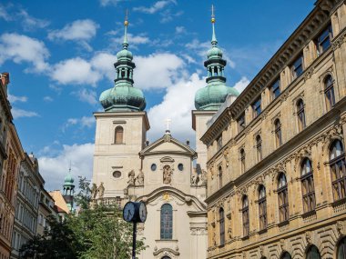 Çek Cumhuriyeti 'nin güneşli bir gününde geleneksel Prag Mimarisi ile Birleştirilmiş Eski Bir Kasaba Sokak Sahnesine Hükmeden Yeşil İkiz Kuleleri olan Tarihi Barok Kilise Binası.
