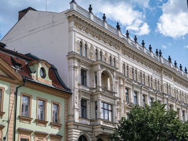 Çek Cumhuriyeti 'nin Parlak Gökyüzü Altındaki Yeşil Yapının yanında Altın Aksanlı Beyaz, Süslü Tarihi Bir Binanın Detaylı Görünümü.