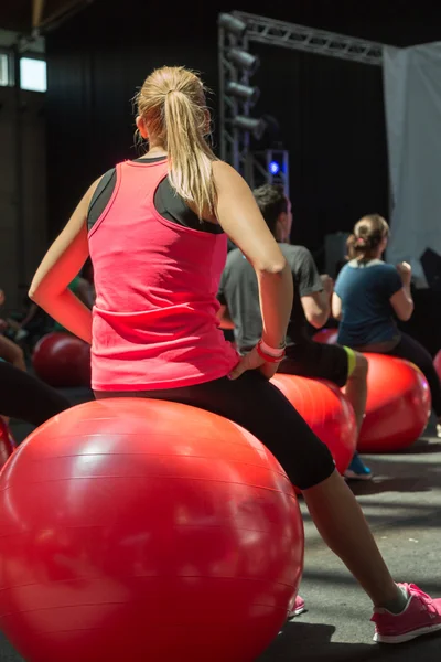 Chica joven rubia haciendo actividad de fitness sentada en una gran bola roja —  Fotos de Stock