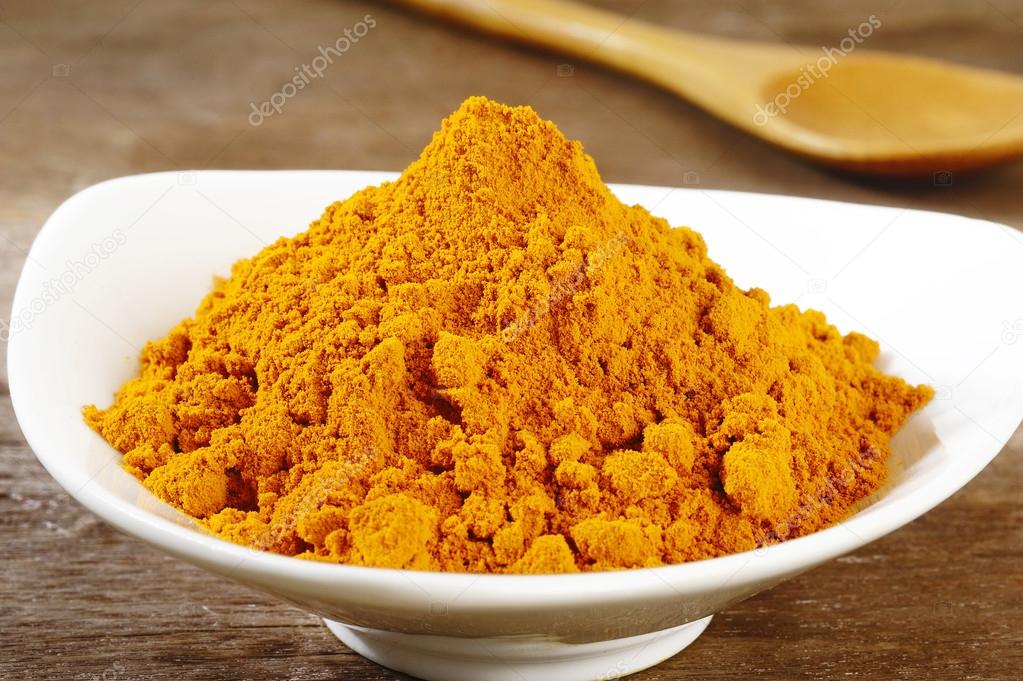 turmeric powder in white dish on wooden background