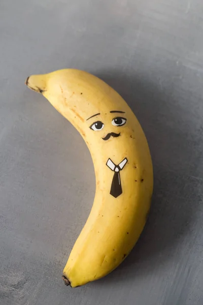 Banánová postava s legrační tvář na gary pozadí. — Stock fotografie
