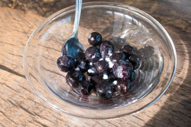 Kaşık ile ahşap masada cam kasede taze yabanmersini.