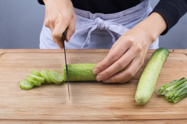 Kapalı kadın elleri kesme tahtasında salatalık kesiyor.