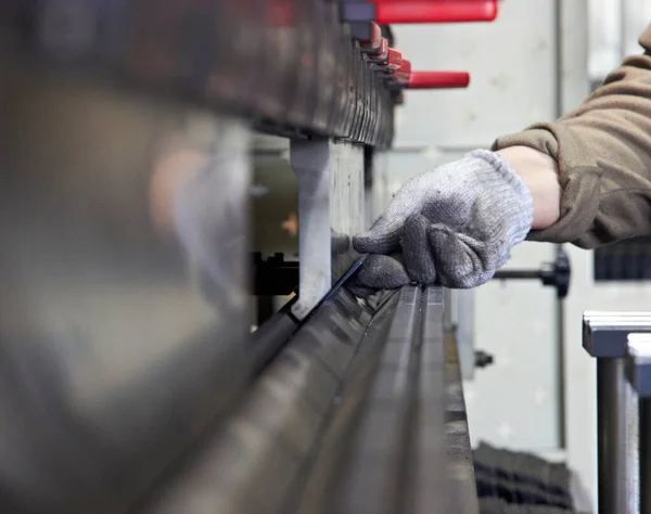 worker produces steel details on a metal bending machine