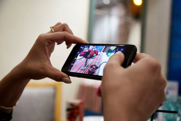 A hand holding a cell phone and making picture of dishes on the table of cafe — Stock Photo, Image