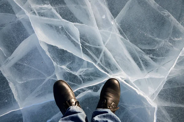 Pies de hombre de pie sobre el hielo transparente de un lago congelado con grietas — Foto de Stock