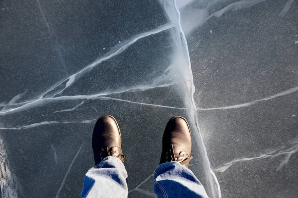 Hombre de pie sobre el hielo transparente con grietas de un lago congelado — Foto de Stock