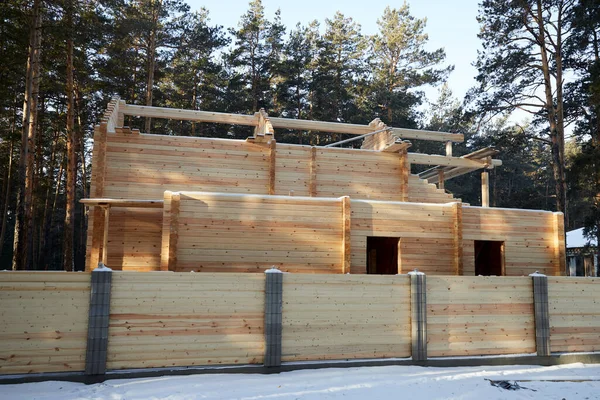 Dům ve výstavbě z dřevěných trámů v lese za slunečného dne s dřevěným plotem — Stock fotografie