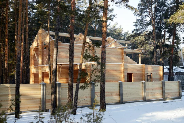 House under construction made of wooden beams in thewinter forest with a wooden fence — Stock Photo, Image