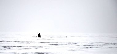 Karla kaplı bir gölün buzunda yalnız bir balıkçı.