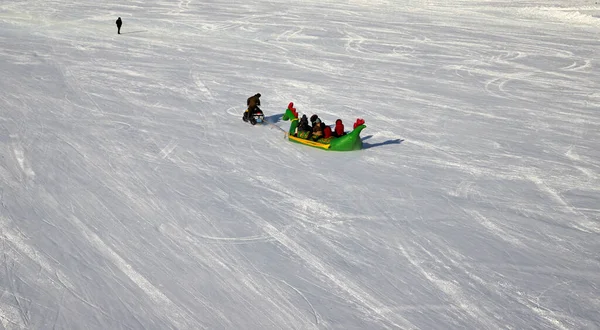 Nur-Sultan, 03 de janeiro de 2021: - snowmobile arrastando banana inflável com pessoas montando no gelo de um rio congelado — Fotografia de Stock