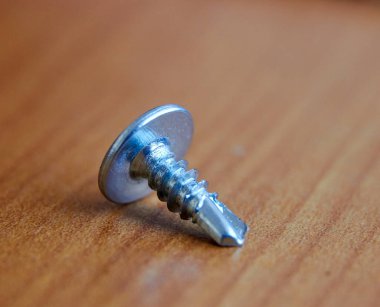 Tahta bir masanın üzerinde galvanize çelikten yapılmış kendi kendine dokunabilen bir vida.