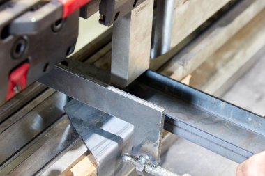 Levha bükme makinesinde metal bir parça tutan işçiler