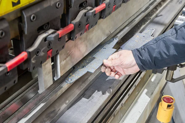Levha bükme makinesinde metal bir parça tutan işçiler