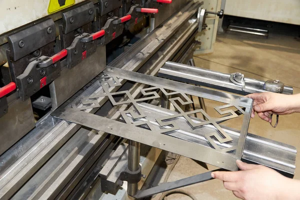 Trabajador sosteniendo una pieza de metal en la máquina dobladora de hojas — Foto de Stock