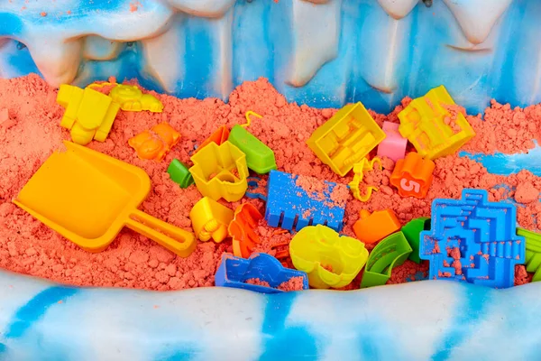 kinetic colored sand and children\'s toys in a plastic sandbox.