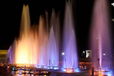 Şehir çeşmesinin fıskiyeleri gece sarı ışıkla aydınlatılıyor.