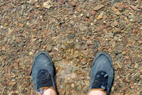 legs of a man standing in clear water with a pebble bottom of the river. natural abstract background