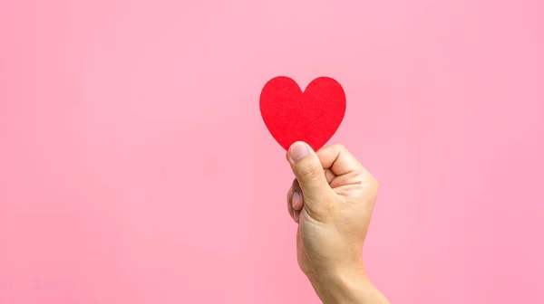 Pembe arka planda kırmızı bir kalbi tutan el..