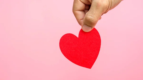 Pembe arka planda kırmızı bir kalbi tutan el..