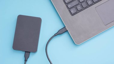 Mavi arkaplandaki bir dizüstü bilgisayara bağlanan siyah harici sabit disk.