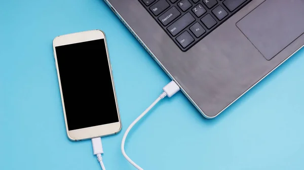 Mavi arka planda dizüstü bilgisayara bağlanan akıllı telefon.