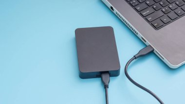 Mavi arkaplandaki bir dizüstü bilgisayara bağlanan siyah harici sabit disk.
