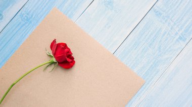 Kahverengi kağıtta kırmızı gül ve mavi ahşap masa.