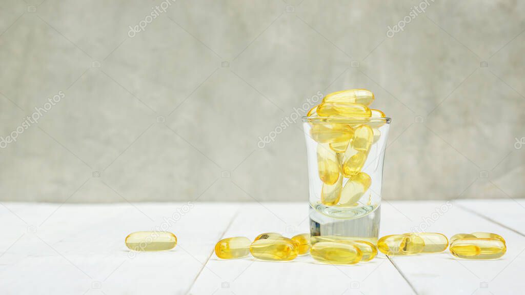 Fish oil in a glass on a white wooden table.