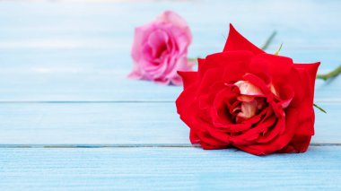 Mavi ahşap bir masada kırmızı gül ve pembe gül.