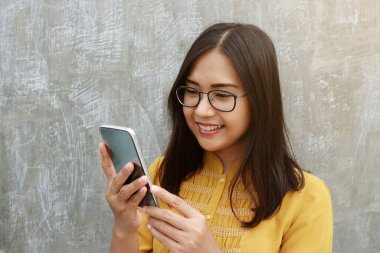 Asyalı kadın gözlük takıyor ve gri arka planda akıllı telefon kullanıyor..