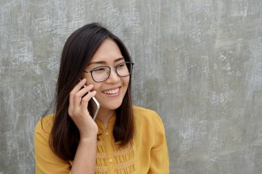 Asyalı kadın gözlük takıyor ve gri arka planda akıllı telefon kullanıyor..