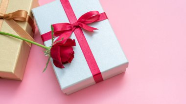 Pembe arka planda kırmızı gül ve hediye kutusu.