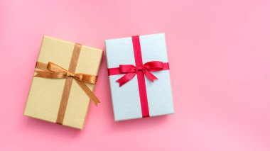 Pembe arka planda gümüş ve altın hediye kutusu.