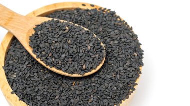 Siyah susam tohumları kaşıkta ve kâse beyaz arka planda..