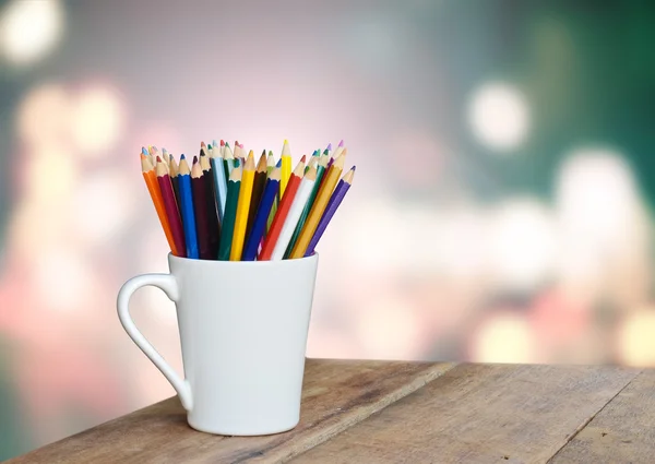 Colored pencils in a glass on wooden background light bokeh — Stock Photo, Image