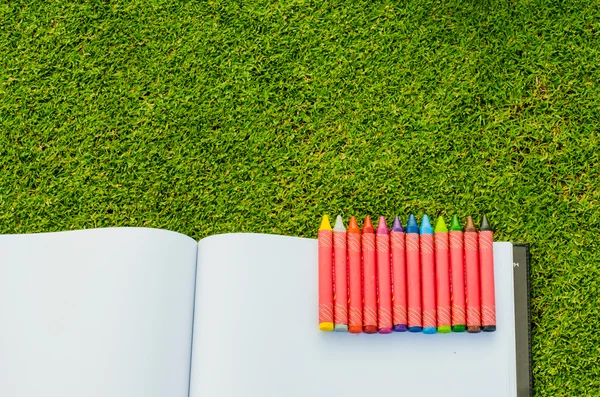 Lápices de cera y cuaderno de bocetos sobre hierba verde primavera fresca — Foto de Stock