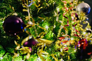 Noel süsleri, gümüş ve mor takılar altın zincirli ve kırmızı ve altın kıvrımlı bir Noel ağacında asılı. Şenlikli bir Noel sahnesi