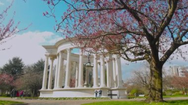 Cardiff, Galler 20 Nisan 2021: İnsanlar güneş ışığının keyfini çıkarıyor ve Galler 'in başkenti Alexandra Gardens' taki Ulusal Savaş Anıtı 'nda yürüyorlar. Ağaçlar çiçeklerle dolu ve gökyüzü mavi..