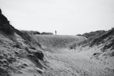 Merthyr Mawr kum tepeleri ve doğa rezervi. Gençler tekrar bir araya gelip kum tepelerini aşıp sırt çantaları, sörf tahtaları ve gün boyu içeceklerle kumsala yürümekten keyif alıyorlar.