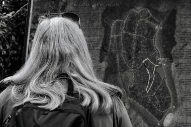 Yaşlı bir kadının siyah beyaz fotoğrafı yerel bir orman patikası için rehber tahtasını kontrol ediyor.