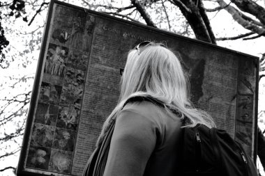 Yaşlı bir kadının siyah beyaz fotoğrafı yerel bir orman patikası için rehber tahtasını kontrol ediyor.