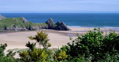 Gower 'daki Three Cliffs Bay' in 4K görüntüsü yükseldi. Galler sahilindeki çarpıcı bir kumlu koy. The Gower Yarımadası 'nın bu popüler turizm merkezinin doğu ucunda üç büyük kaya duruyor.