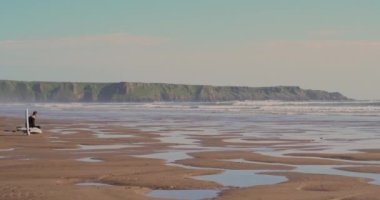 Llangennith, Gower Yarımadası 'nın güneybatı Galler' de harika bir sörf plajı. Güneş, Galler 'in Swansea yakınlarındaki Gower Yarımadası' ndaki Llangennith Sahili 'nde dalgaların üzerine ışıldıyor. Dalgalarda sörf yapan sörfçülerin suya düştüğünü görebilirsiniz..
