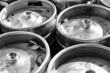 Depoya yüklenmeyi bekleyen metal bira fıçılarının siyah beyaz fotoğrafı.