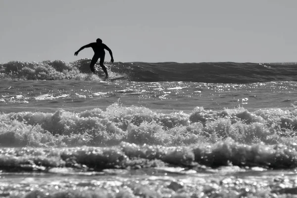 パワー半島のLlangennithビーチで波に乗るサーファーのシルエット画像 砂浜と波の圧延とウォータースポーツ活動のための人気のあるスポーツ 太陽が水の上で輝く — ストック写真
