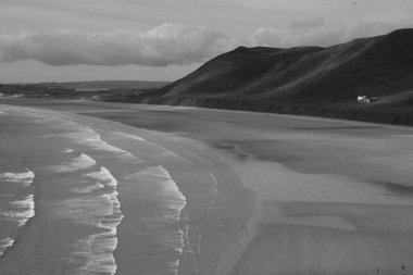 Gower Yarımadası 'ndaki Worm' s Head 'deki uçurum yüzeyi altın kum ve dalgaların aktığı Llangennith' teki muhteşem sahili incelemek için mükemmel bir görüş açısı sunuyor. İnsanlar manzaranın tadını çıkarıyor